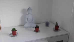 Ein weißes Regal mit einer Buddha-Statue, drei Topfpflanzen und einer Kerze.