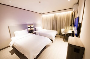 A hotel room with two beds, a desk, a chair, a TV, and a trash bin.
