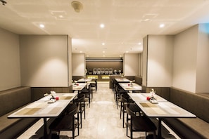 A hotel dining area with tables and chairs, a reception desk, and a counter with various items.