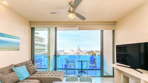 A modern living room with a sofa, a TV, and a balcony with a view of buildings and a beach. - Sabor A Miel by Stella Rentals (Playa del Carmen)