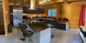Une cuisine moderne dotée d’un îlot central, de tabourets de bar noirs, d’un évier en acier inoxydable et de murs en bois.