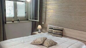 Un dormitorio con una cama grande, una mesita de noche con lámpara, una ventana con persianas y una pared con textura.