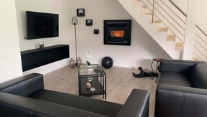 Una sala de estar moderna con un televisor de pantalla plana, una chimenea, una escalera y sofás de cuero negro.