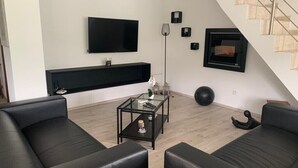 Una sala moderna con televisor de pantalla plana, chimenea, escalera y sofás de cuero negro.