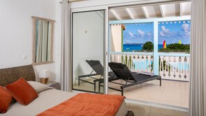 Habitación de hotel con cama, mesita de noche, lámpara y vista a un balcón con piscina y playa.