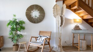 Una habitación acogedora con una mecedora, una planta en maceta, un espejo montado en la pared y una lámpara sobre una mesa.
