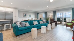 Ein geräumiges Wohnzimmer mit einem türkisfarbenen Sofa, Holzboden und Deckenventilator.