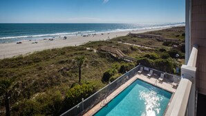 Blick vom Pool auf einen Strand mit Holzterrasse und Liegestühlen.