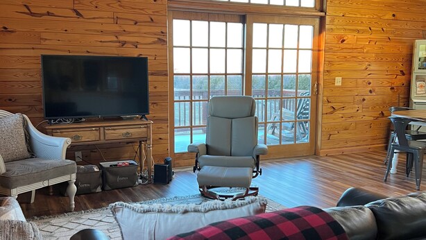 A cozy living room with wooden walls, a large window, a television, and comfortable seating.