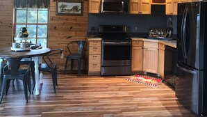 A wooden-paneled kitchen with built-in appliances, a dining area with chairs, and a window with a view.