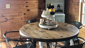 A wooden-paneled room with a round wooden table, black chairs, and a cabinet with glass doors.