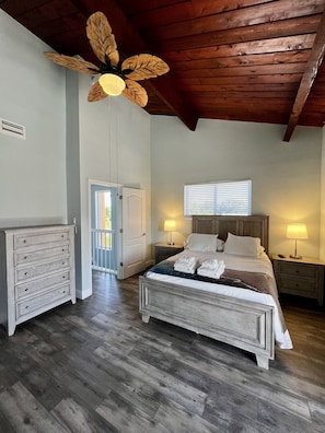 A bedroom with a bed, bedside tables, a dresser, a ceiling fan, and a window.