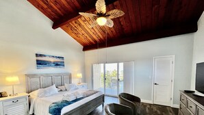 A bedroom with a wooden ceiling, a bed with white linens, a chair, a TV, and a view through the door. - Spacious condo, great location in paradise! (Key Largo)