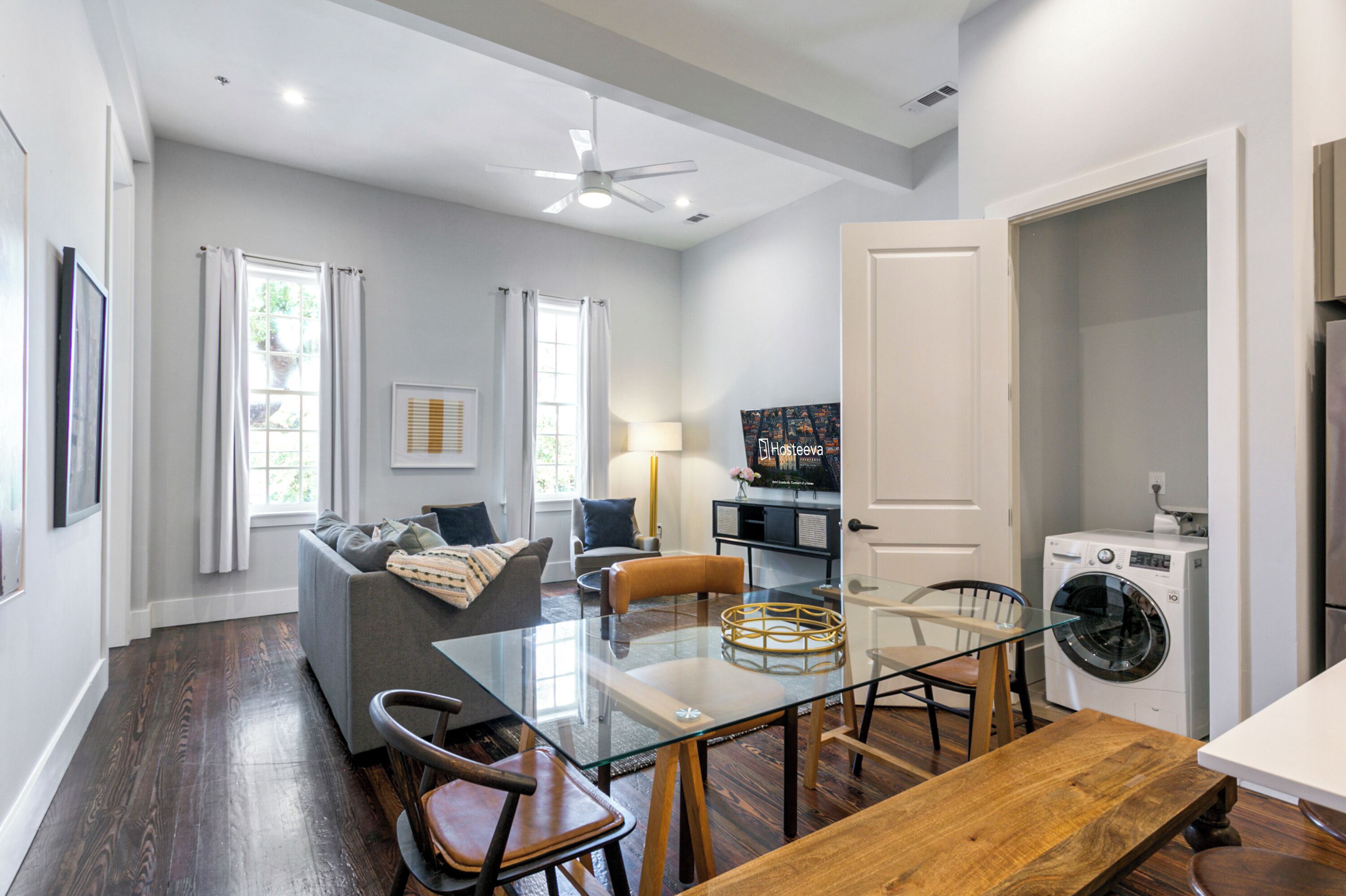 A modern kitchen with a built-in washer and dryer, a dining area with a glass table, and a living room with a sofa and a TV.
