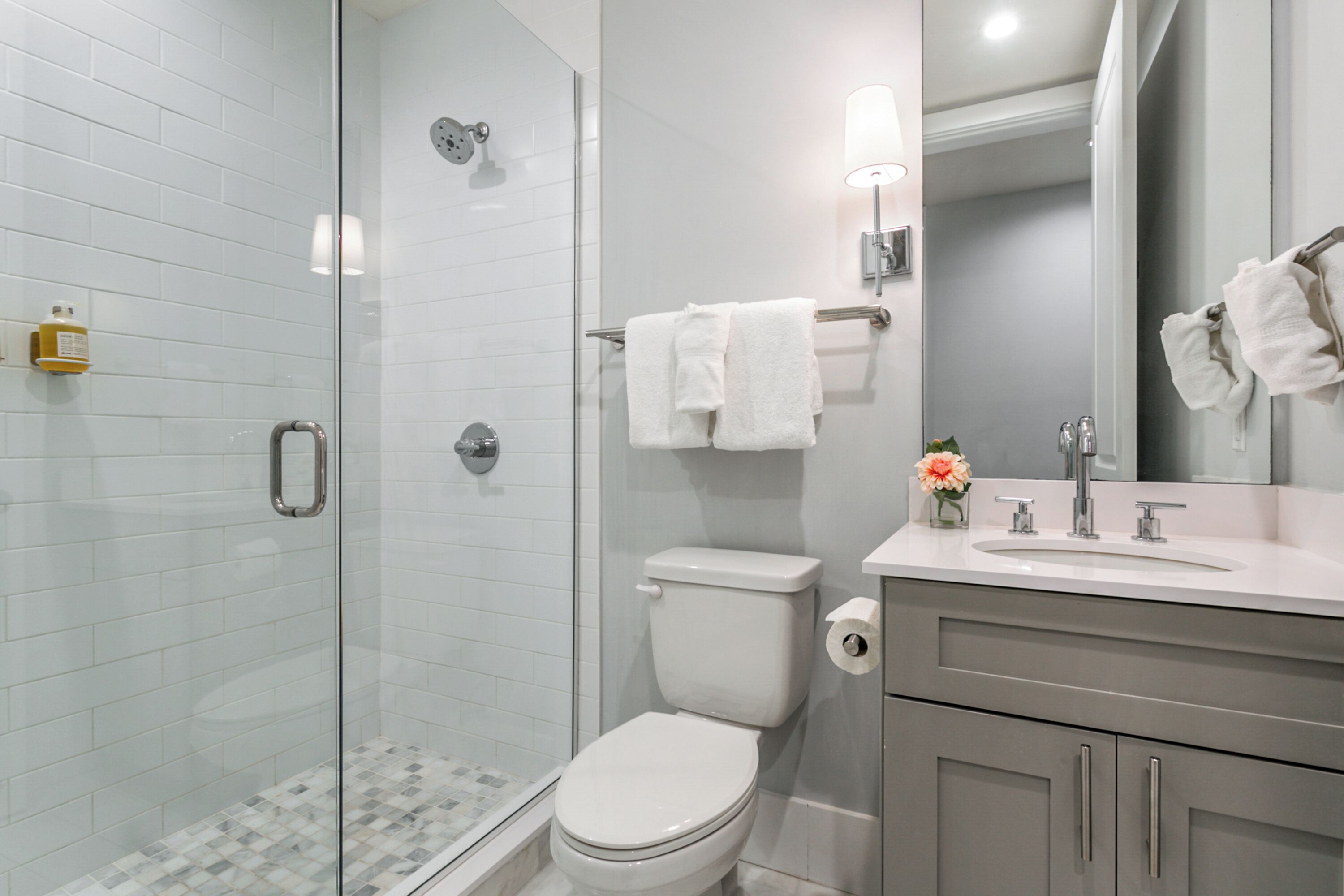 A modern bathroom with a glass shower enclosure, a toilet, a sink with a mirror, and a towel rack.