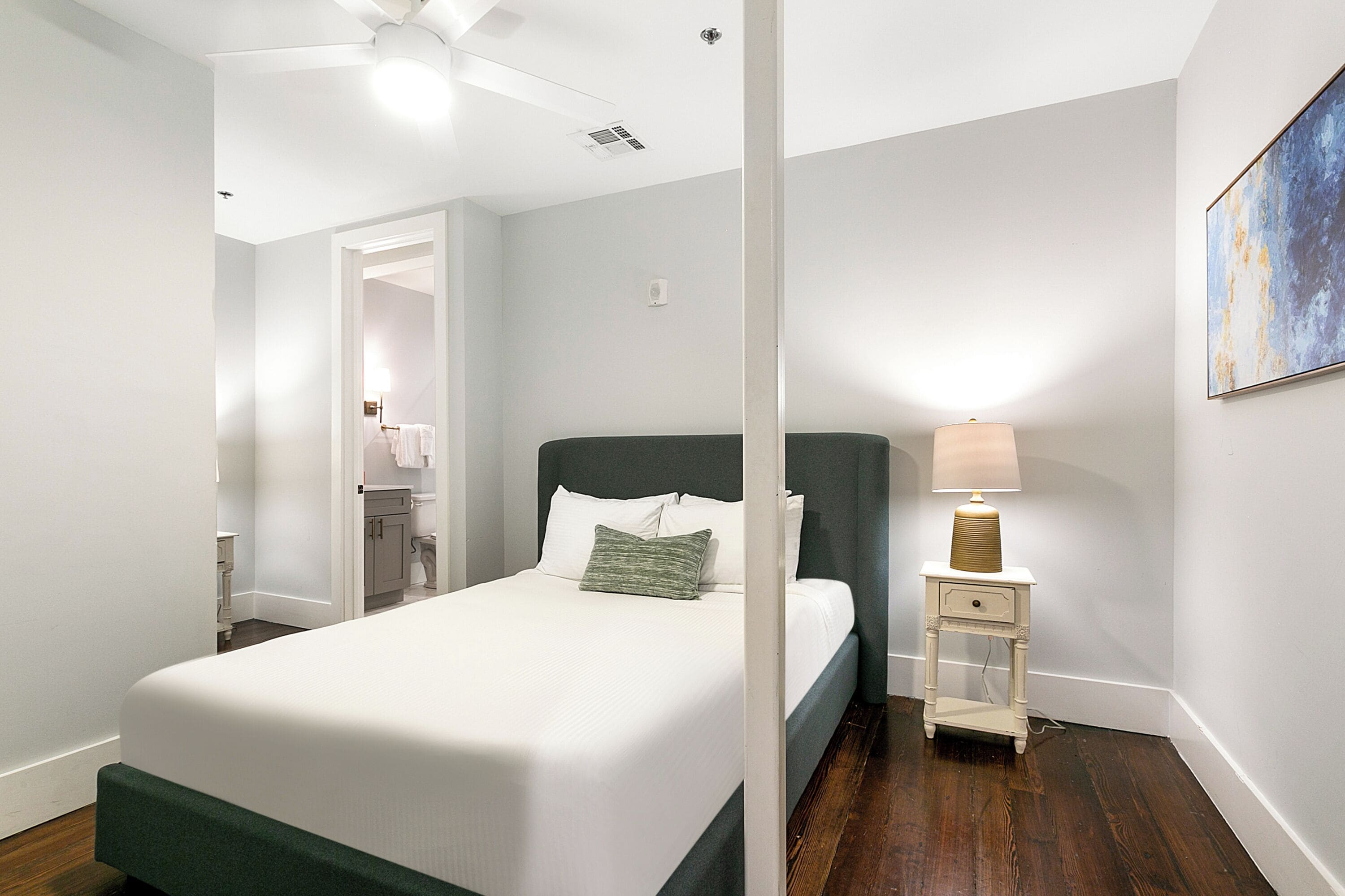 A bedroom with a bed, a nightstand, a lamp, and a painting on the wall.