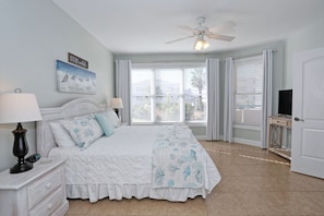 A bedroom with a bed, nightstands, a ceiling fan, a TV, and a window with blinds.