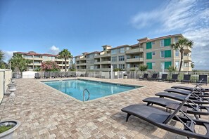 A hotel pool area with a rectangular pool, lounge chairs, and a building with balconies.