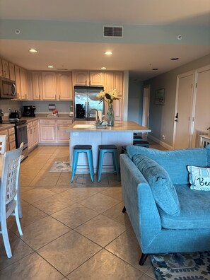 A modern kitchen with a central island, bar stools, and a blue sofa in a living area.