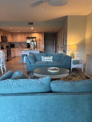 A living room with a blue sofa, a coffee table, and a kitchen in the background.