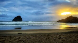 Une plage avec une grande formation rocheuse et un coucher de soleil.