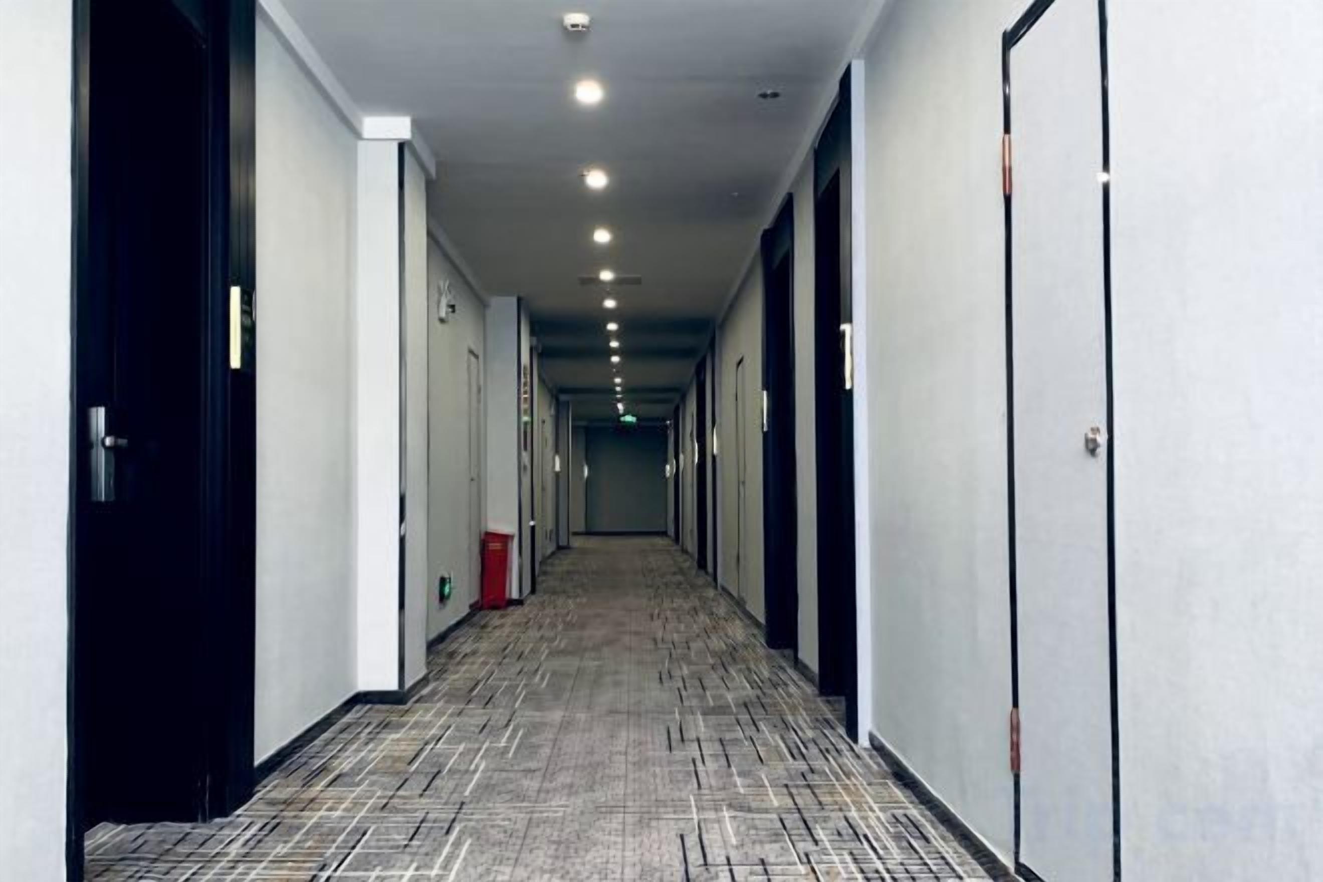 A hotel corridor with doors on both sides, a patterned carpet, and a trash bin.