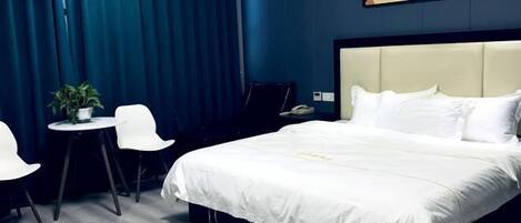 Habitación de hotel con una cama grande, una mesita con sillas, una planta en maceta y un cuadro en la pared.