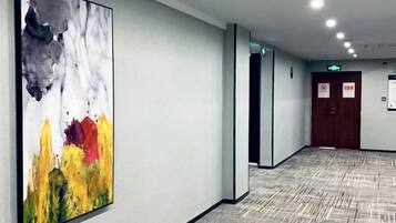 Un pasillo con un cuadro abstracto grande, una alfombra estampada y una puerta con un cartel.