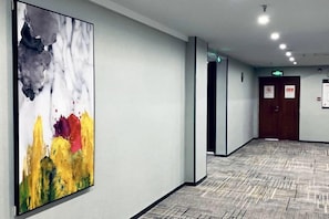 A hallway with a large abstract painting, a patterned carpet, and a door with a sign. - Saijia Hotel (Rugao Rt Mart) (Rugao)