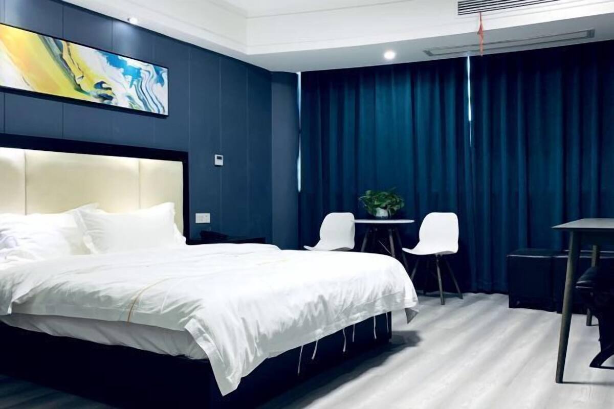 Moderni hotellihuone, jossa on suuri sänky, työpöytä, kaksi tuolia, pieni pöytä ja taulu seinällä.