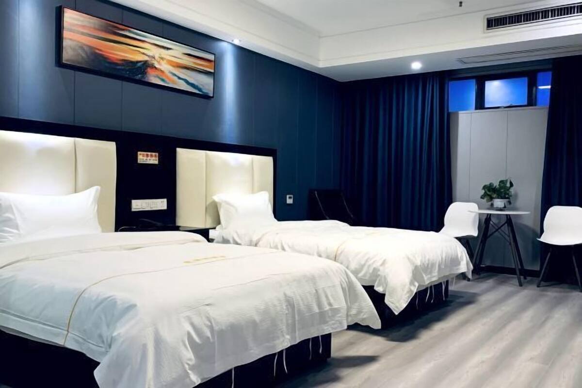 Hotellihuone, jossa on kaksi sänkyä, työpöytä, tuoleja, pieni pöytä, jossa on kasvi, ja taulu seinällä.