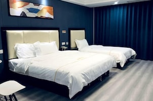 Habitación de hotel con dos camas, una silla blanca, un cuadro en la pared y una cortina azul oscuro.