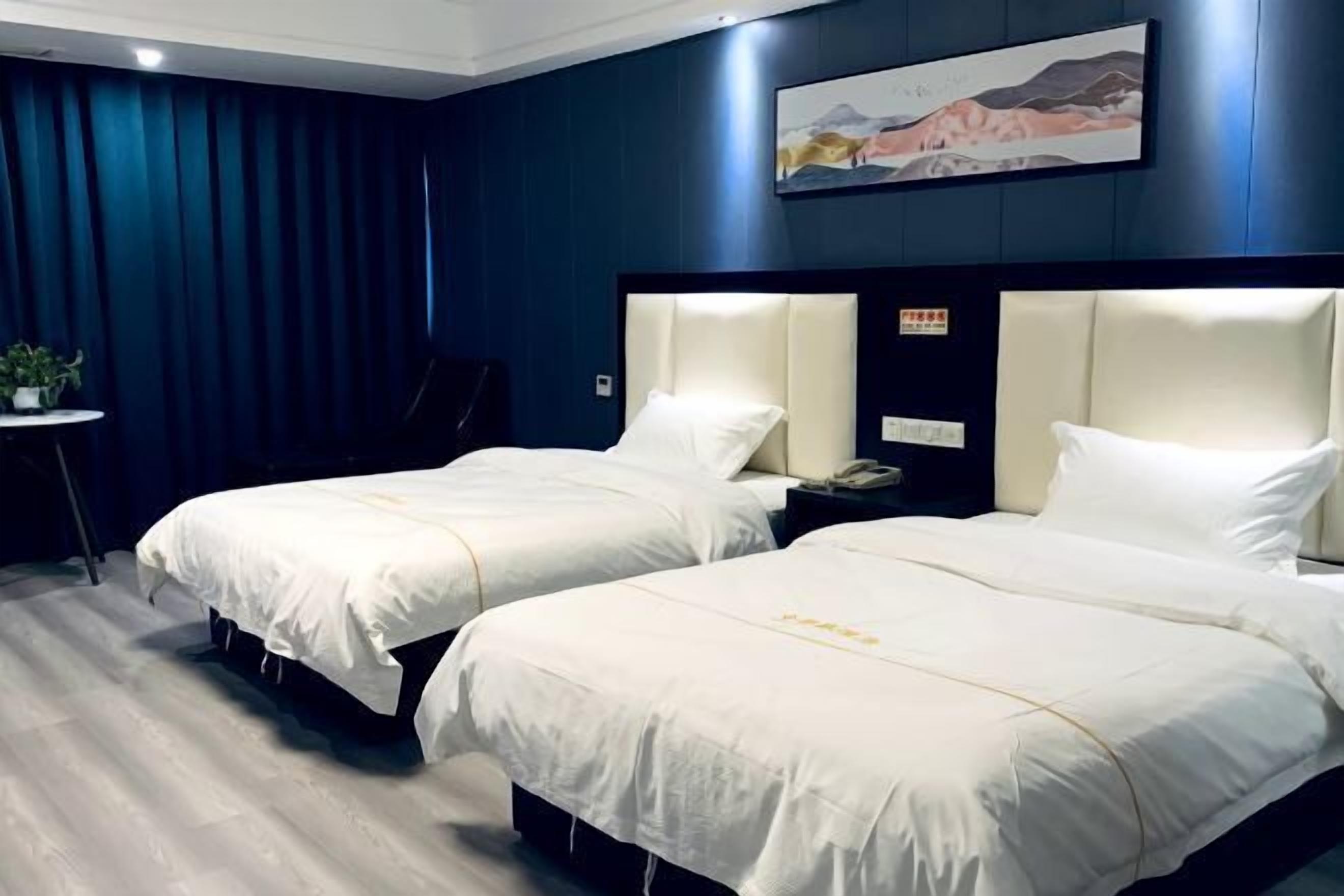 A hotel room with two beds, a small table with a plant, and a painting on the wall.