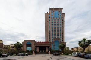 Un hotel alto con una entrada central, varios pisos y un estacionamiento con varios autos.