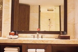 Un baño con un espejo grande, un lavamanos con dos grifos y un perchero con toallas dobladas.