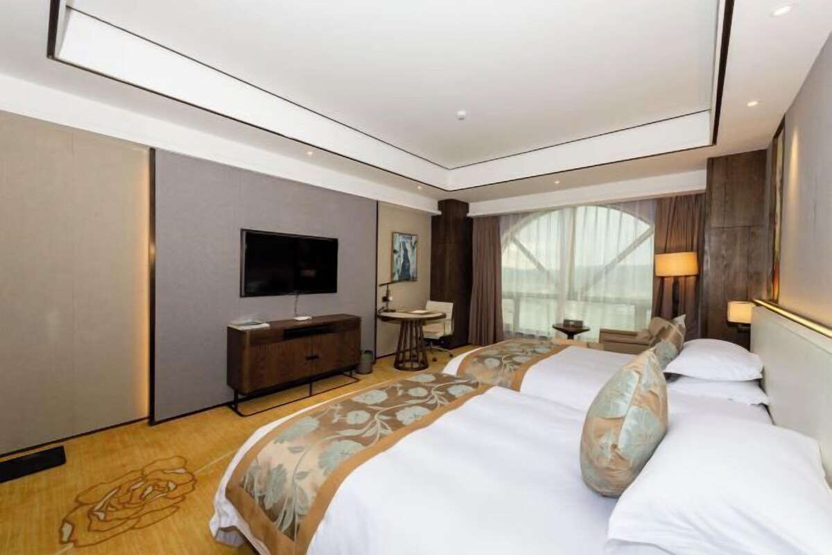 A hotel room with a large bed, a desk, a TV, and a window with curtains.