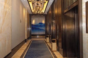 A hotel hallway with a marble floor, a blue carpet, a chandelier, and a door with a mountain view mural.