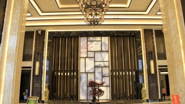A lobby with a chandelier, a large decorative panel, and a potted plant.