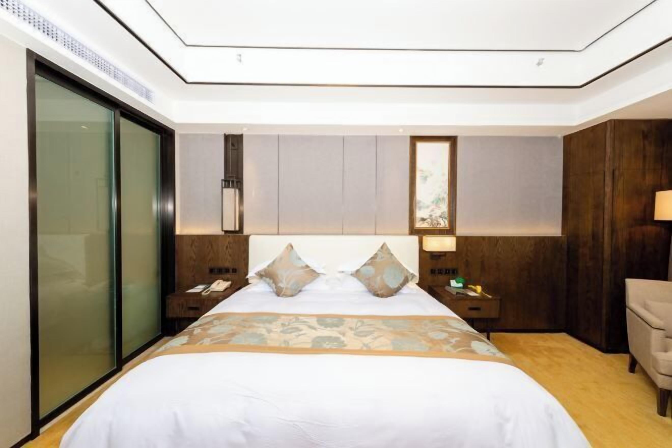 Ett modernt hotellrum med en stor säng, ett träbeklätt sänggavel och en glasdörr.