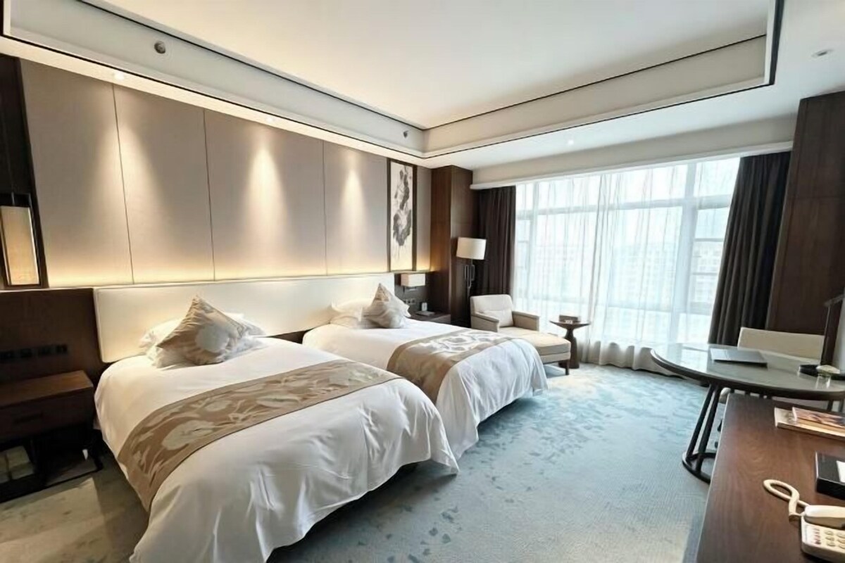 Une chambre d’hôtel avec deux lits, un bureau et une grande fenêtre.