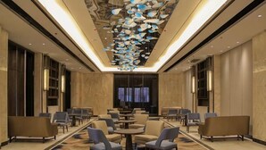 A hotel lobby with a central seating area, a chandelier, and a large window.