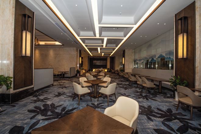A hotel lobby with a long reception desk, multiple seating areas, and a large window with a view.