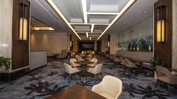 A hotel lobby with a long reception desk, multiple seating areas, and a large window with a view.