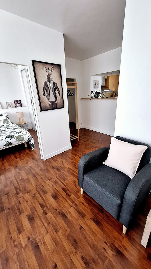 Sala moderna com sofá cinza, uma obra de arte com zebras emoldurada, piso de madeira e vista para a área da cozinha.