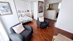 A modern living room with a bed, two armchairs, and a large mirror.