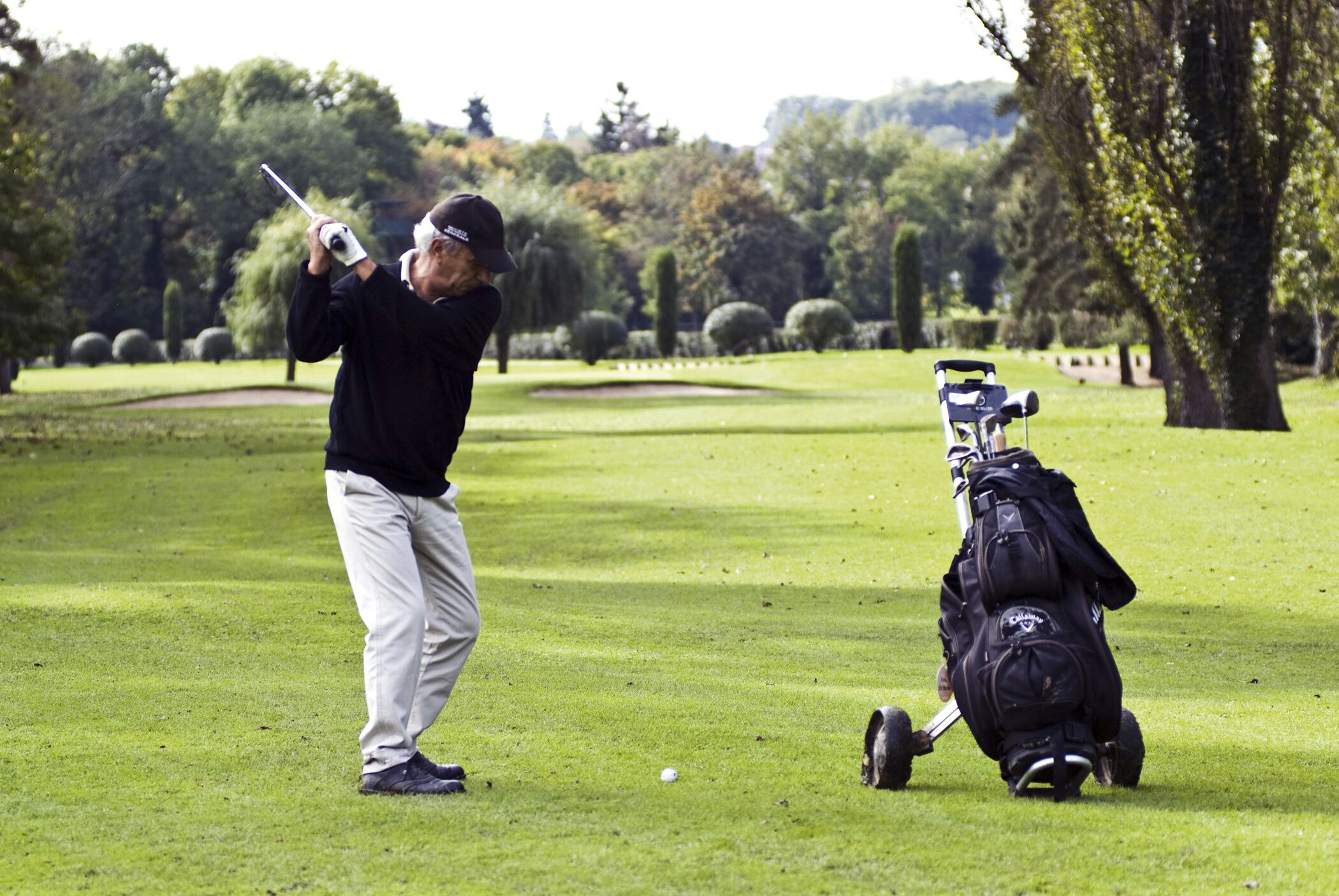Une personne se trouve sur un terrain de golf, tenant un club de golf, avec un sac de golf à proximité.
