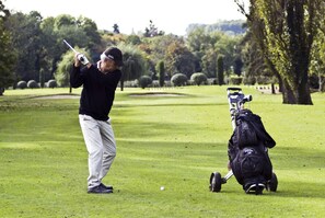 Una persona en un campo de golf sosteniendo un palo de golf, con un bolso de golf cerca.