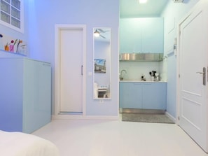 A compact room with a bed, a small kitchenette, and a door leading to another room.