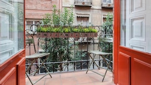 Ein Balkon mit Metallgeländer, zwei Stühlen und einem Blumentopf mit Grünpflanzen.