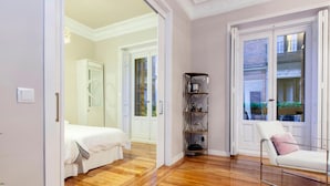 Ein Hotelzimmer mit Holzboden, einem Bett, einem Sessel, einem Regal und einer Tür, die auf einen Balkon führt.